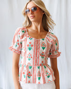 Woman wearing a floral embroidered blouse and sunglasses against a white background