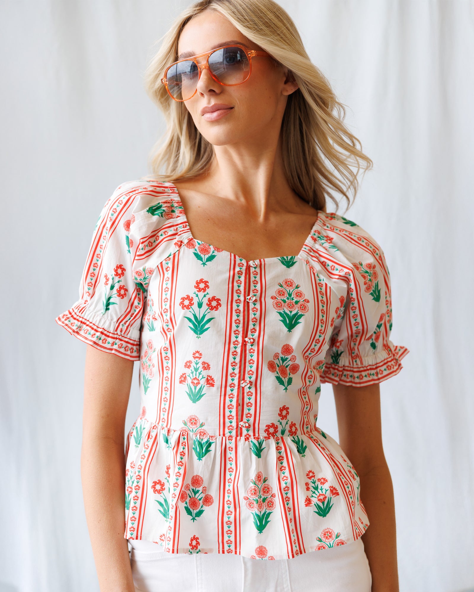 Woman wearing a floral embroidered blouse and sunglasses against a white background