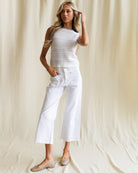 Woman wearing a white sleeveless top and white pants against a beige background