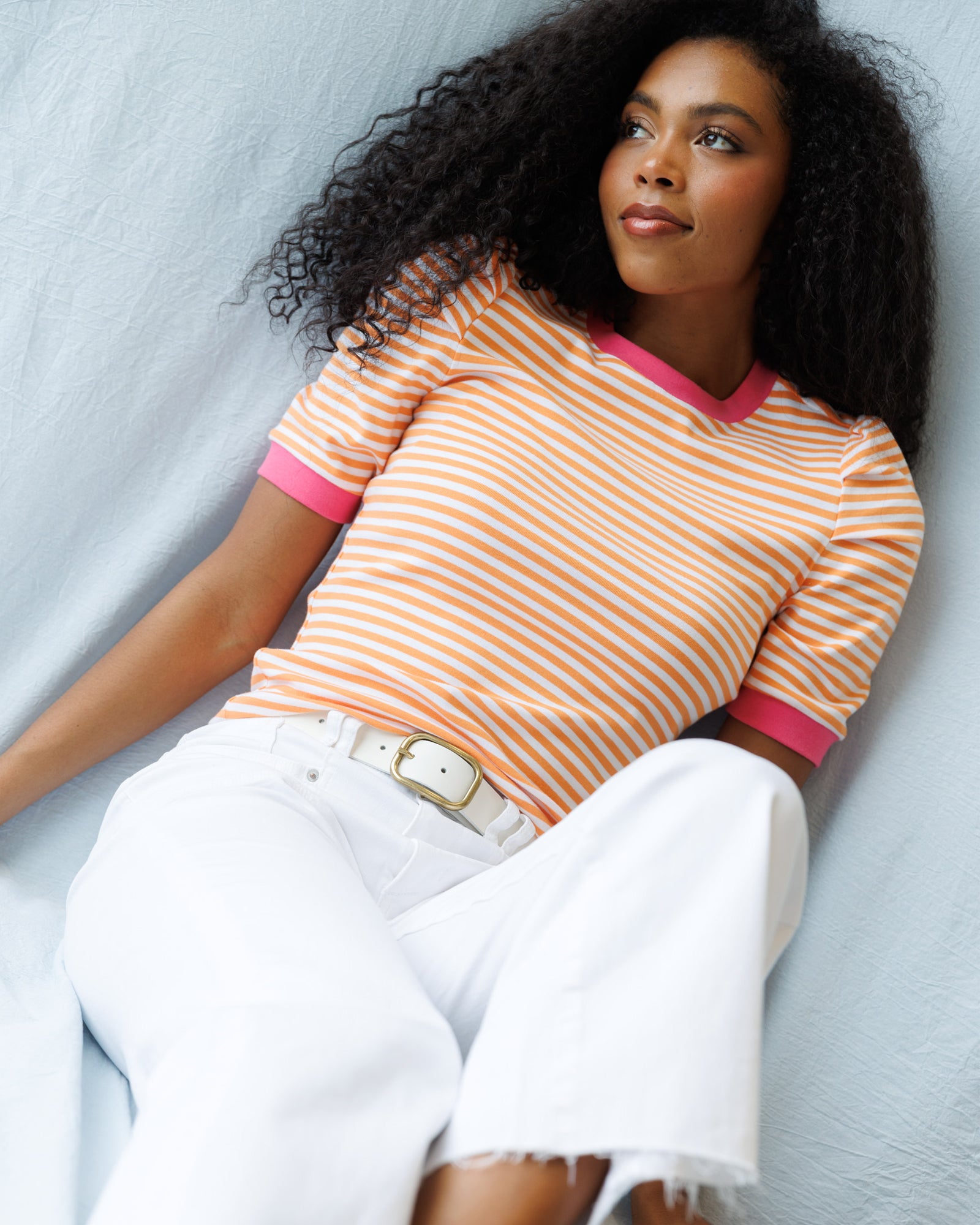Woman wearing a striped shirt and white pants against a light background
