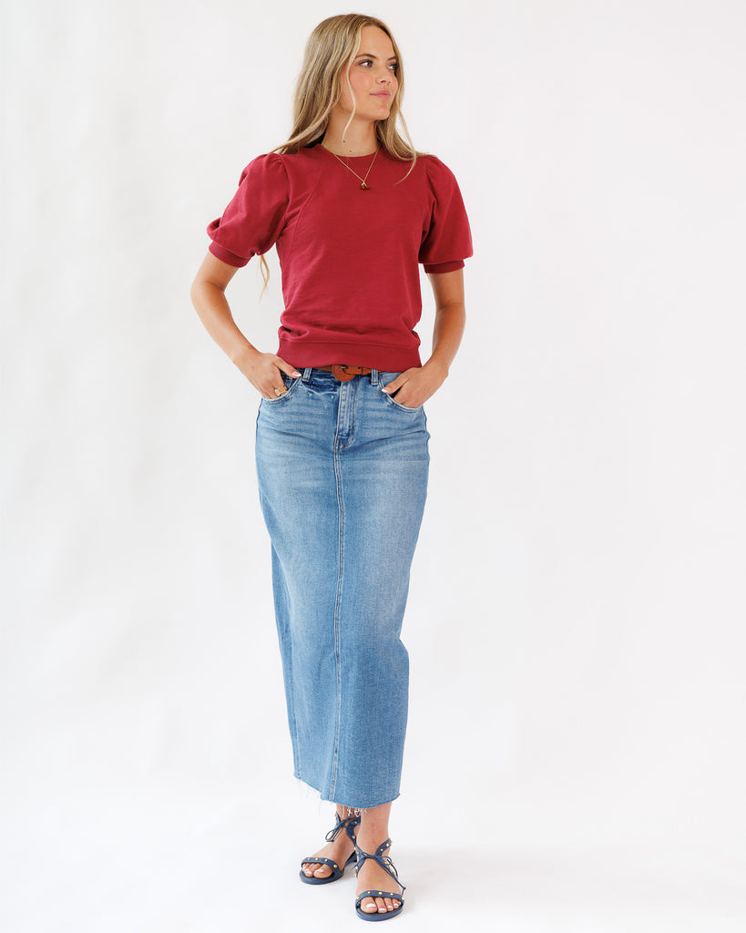 Woman wearing a red top and a blue denim maxi length skirt on a white background