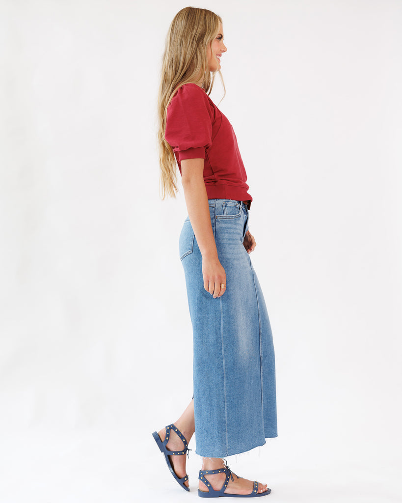 Woman wearing a red top and a blue denim maxi skirt on a white background