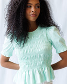 Woman wearing a light green smocked top against a plain background