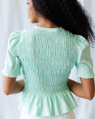 Person wearing a light green smocked blouse against a white background