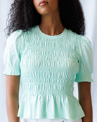 Woman wearing a light green smocked blouse against a white background