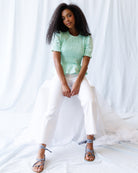 Woman wearing a light green top and white pants sitting on a white fabric background