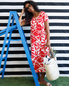 Woman in a red floral dress standing next to a blue ladder against a black and white striped wall.