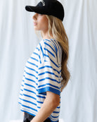 Person wearing a black cap and blue and white striped shirt against a white curtain background