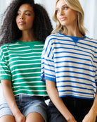 Two women wearing striped shirts sitting side by side.
