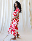 Woman wearing a red and white patterned dress standing against a white curtain.