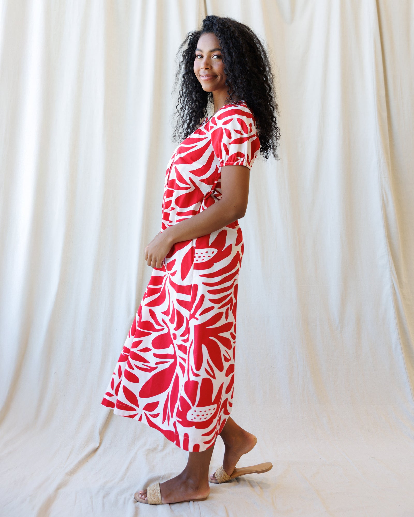 Woman wearing a red and white patterned dress standing against a white curtain.