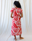 Woman wearing a red and white floral dress against a white curtain background