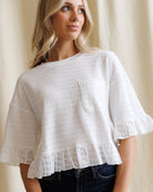 Woman wearing a white blouse with lace details against a beige curtain background