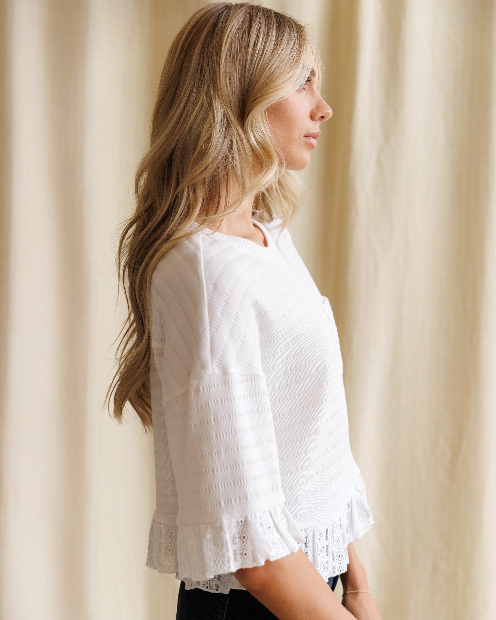 Woman wearing a white blouse with lace details against a beige curtain background