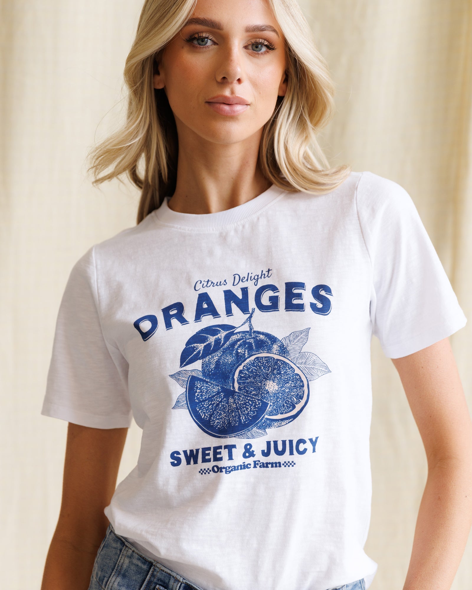Woman wearing a white t-shirt with blue 'Oranges' graphic design.