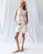 Woman wearing a sleeveless floral top and white shorts against a white background