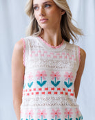 Woman wearing a sleeveless crochet top with floral patterns on a plain background