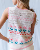 Woman wearing a sleeveless knitted top with floral patterns on a light background