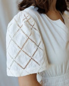 White lace shrug over a plain white top against a neutral background