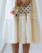 Person wearing a white lace dress holding a polka dot clutch with floral accents.
