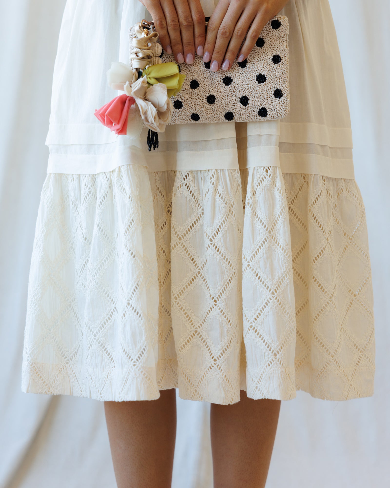Person wearing a white lace dress holding a polka dot clutch with floral accents.