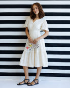 Woman in a white dress standing against a black and white striped wall.