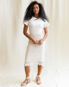 Woman wearing a white lace skirt over a white top against a plain background
