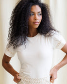 Woman wearing a white blouse with lace details against a neutral background