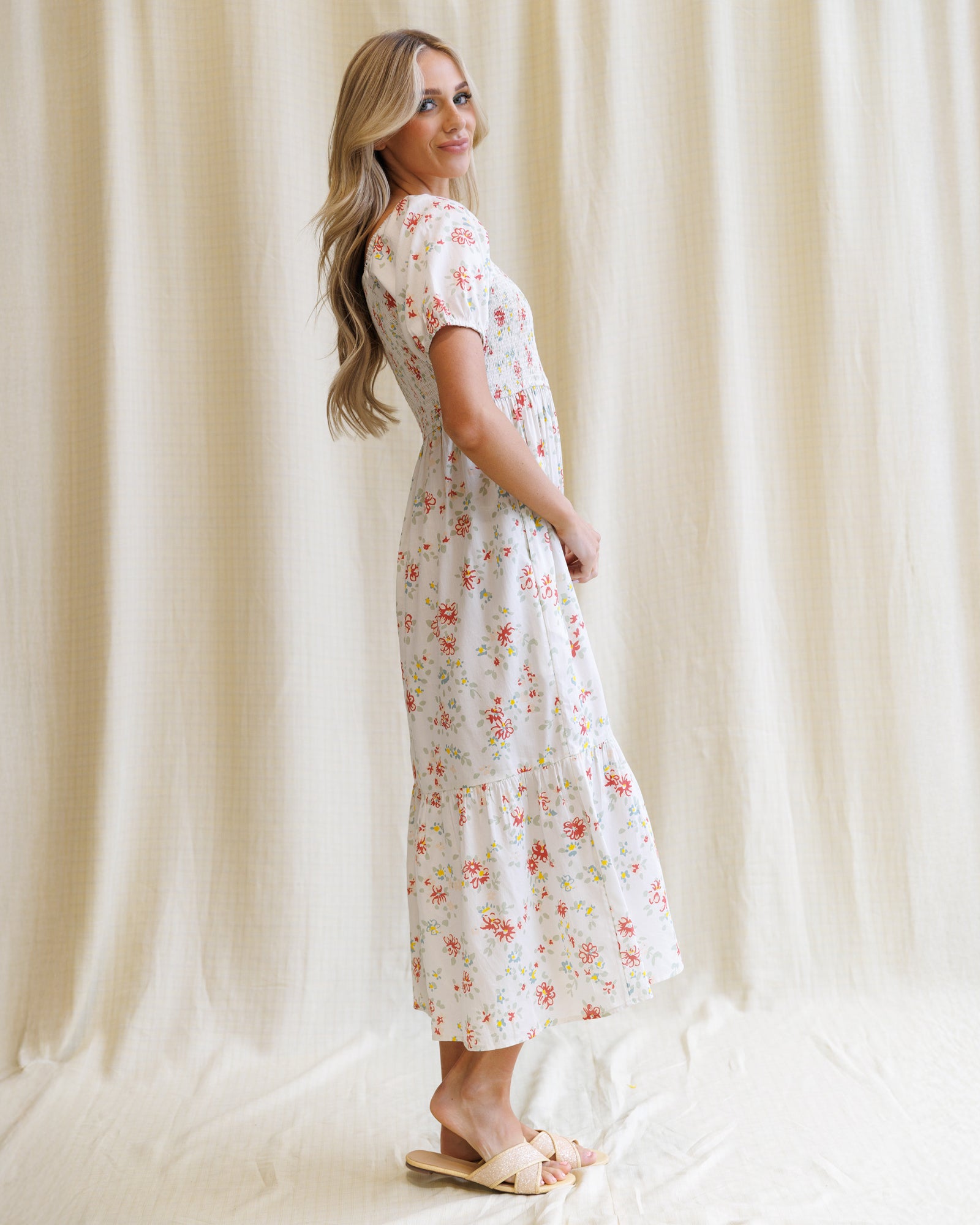 Woman wearing a floral dress standing against a white curtain