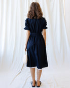 Woman wearing a black dress against a white curtain backdrop