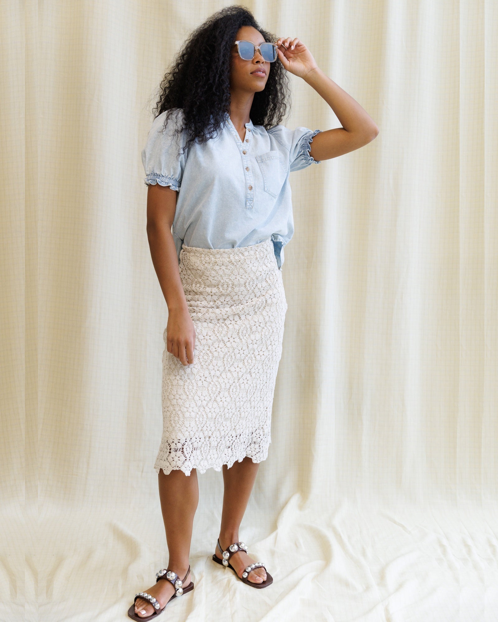 Woman wearing a light blue shirt and white lace skirt against a neutral background