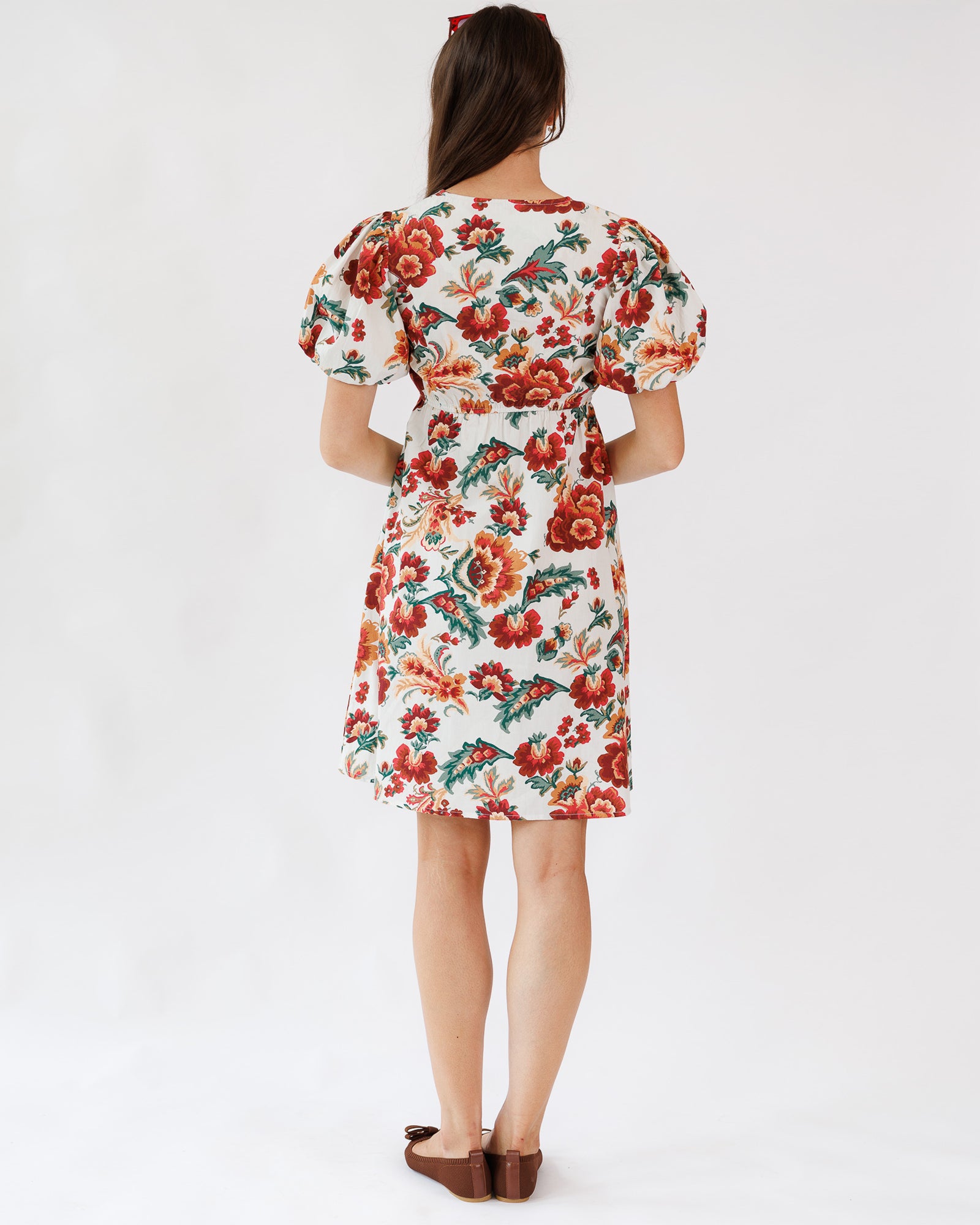 Model wearing a white with red, orange and green floral printed short sleeve knee length dress on a white background.