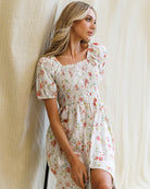 Woman wearing a floral dress standing against a neutral background