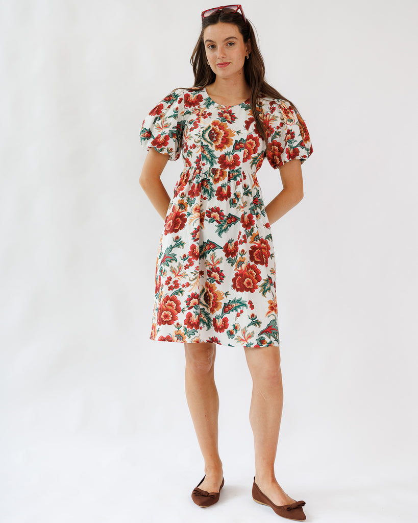 Model wearing a white with red, orange and green floral printed short sleeve knee length dress on a white background.