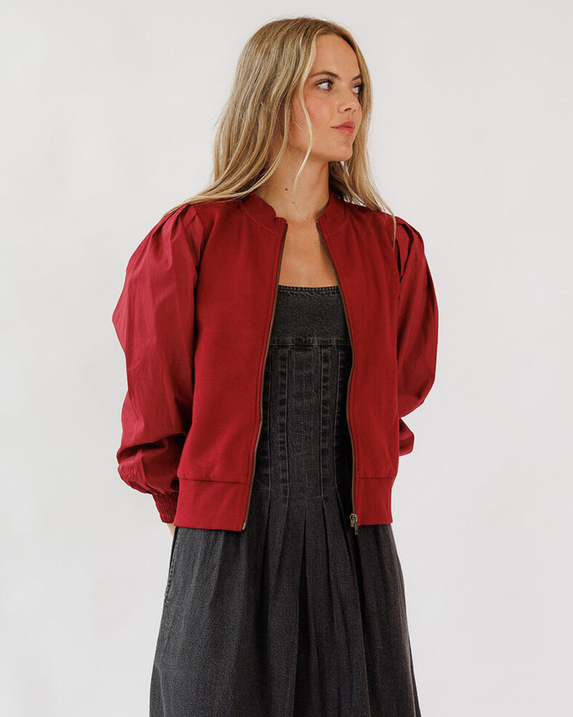 Woman wearing a red bomber jacket over a black dress on a white background