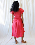 Person wearing a pink dress standing against a white curtain