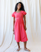 Woman wearing a pink dress against a white curtain background