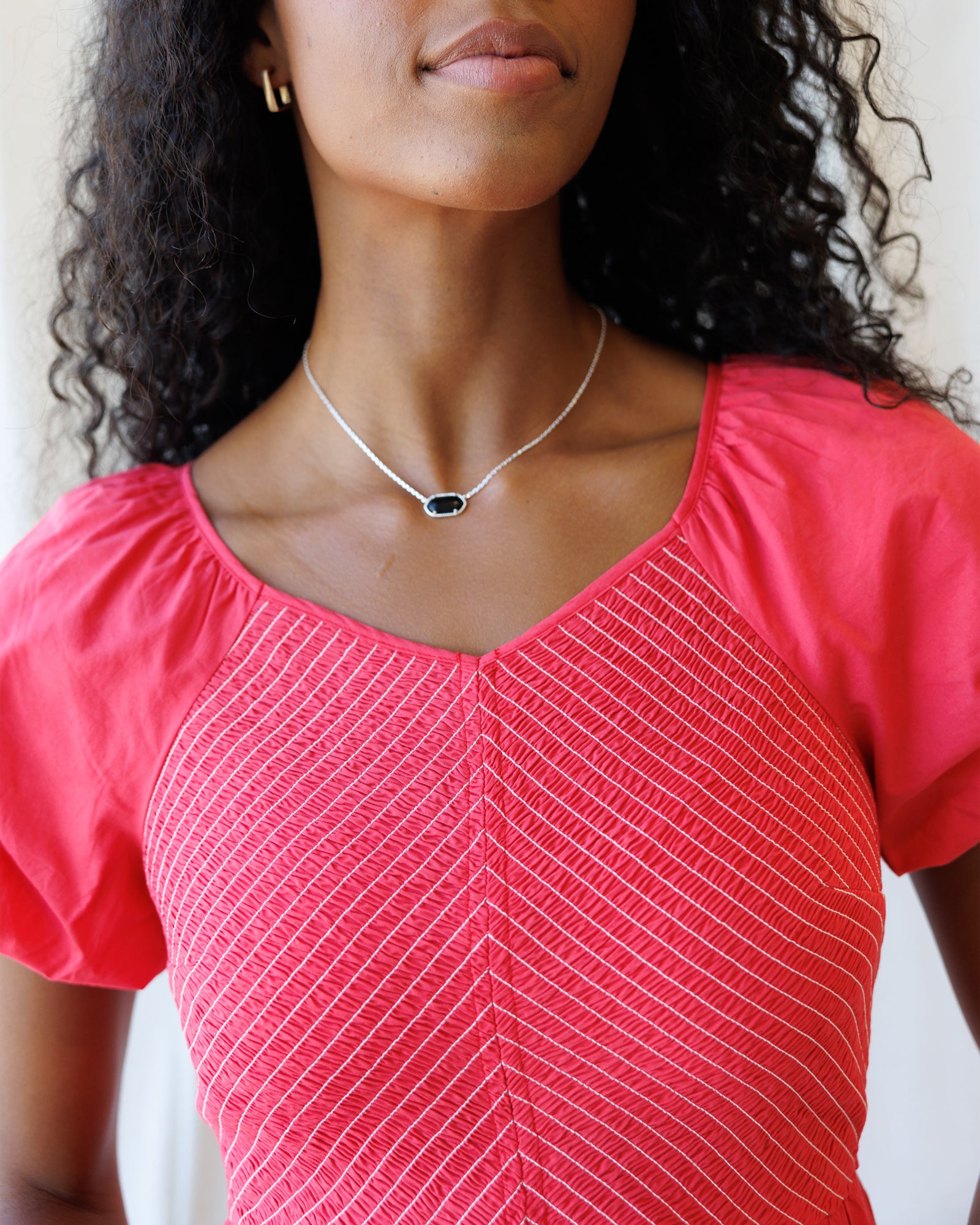 Woman wearing a pink top with a subtle pattern and a silver necklace.