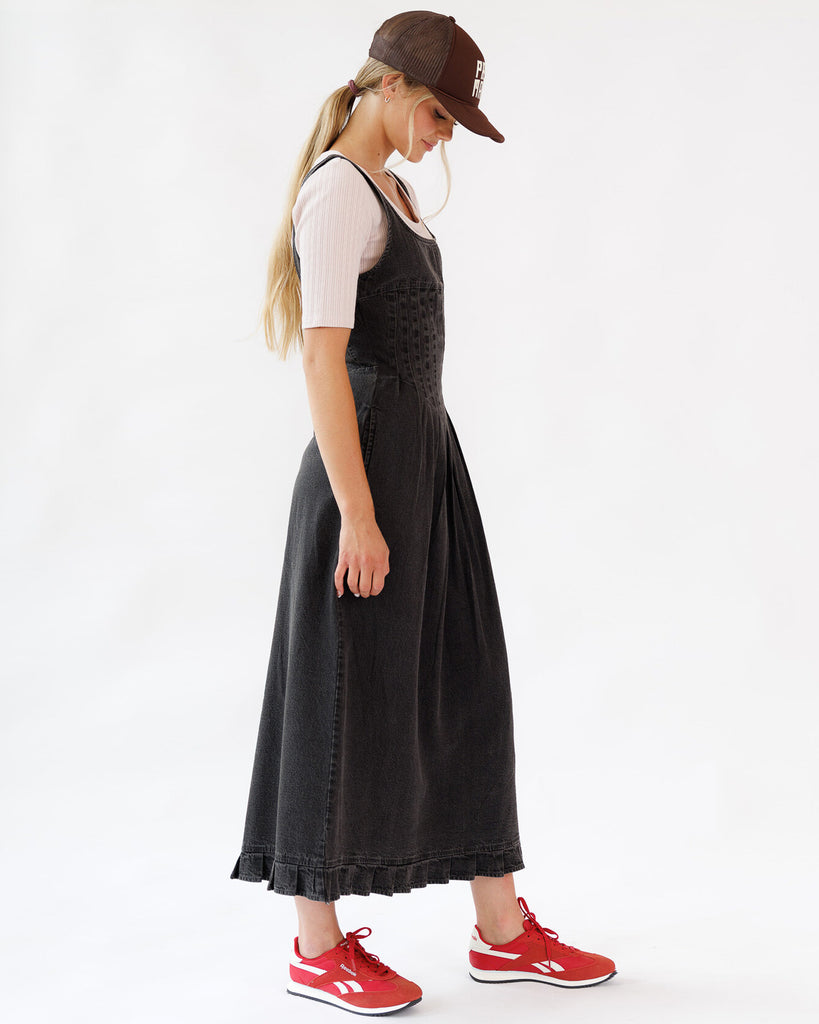 Woman wearing a black dress, white shirt, red sneakers, and brown cap on a white background
