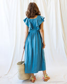 Woman wearing a blue dress with ruffled sleeves against a white curtain background