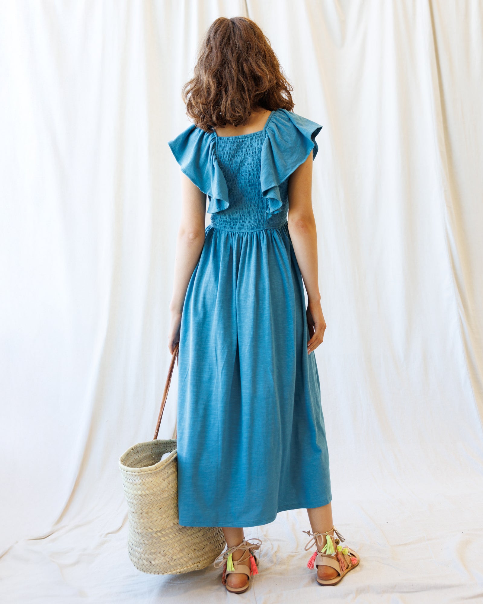 Woman wearing a blue dress with ruffled sleeves against a white curtain background