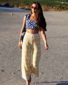 Woman in a blue and white patterned top and yellow and white striped pants walking on a beach.