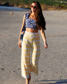 Woman in a blue and white patterned top and yellow and white striped pants walking on a sandy beach.
