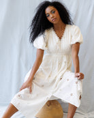Woman wearing a white dress with floral cutouts against a light background