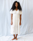 Woman wearing a white dress with floral embroidery against a plain background