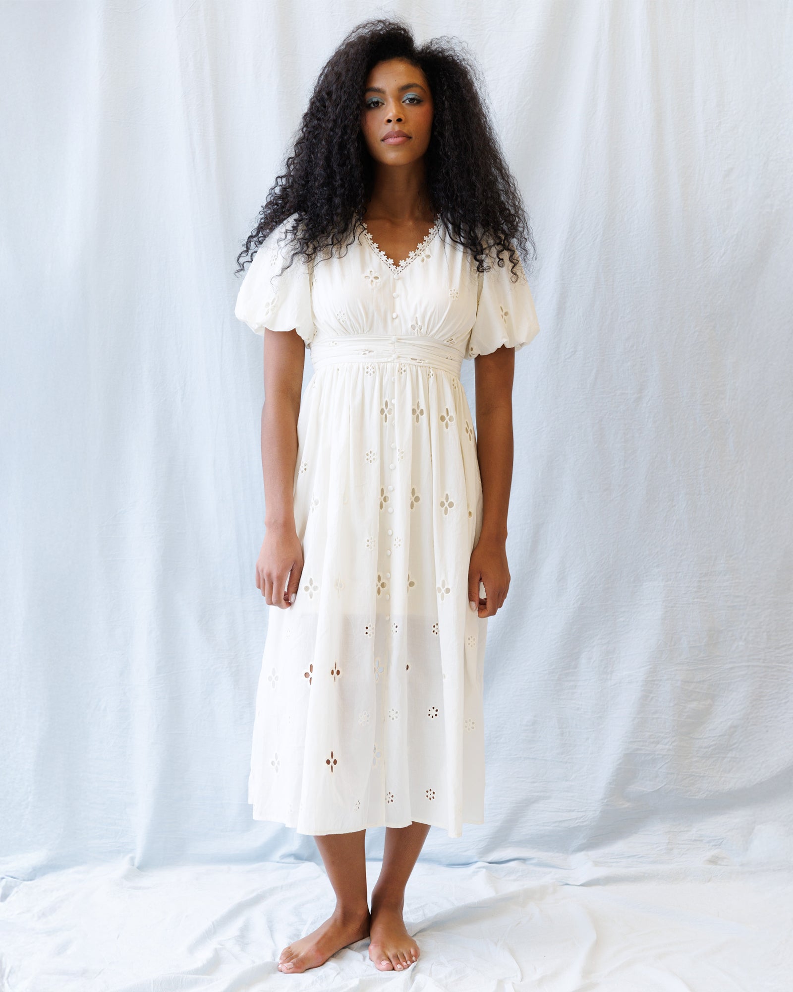Woman wearing a white dress with floral embroidery against a plain background
