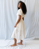Woman wearing a white dress with floral patterns against a plain background