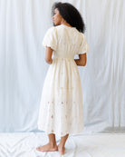 Woman wearing a white dress with intricate patterns against a plain background