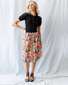 Woman wearing a black top and colorful floral skirt against a white background