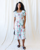 Woman wearing a floral dress standing against a white curtain